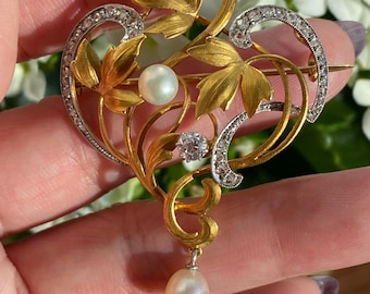 May include: A gold and silver brooch with a floral design. The brooch features two pearls and a diamond. The brooch is in the Art Nouveau style.