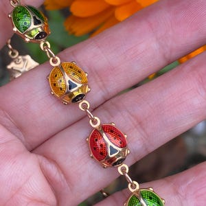 May include: A gold chain bracelet with a series of enamel ladybug charms. The ladybugs are red, green, and yellow with black spots.