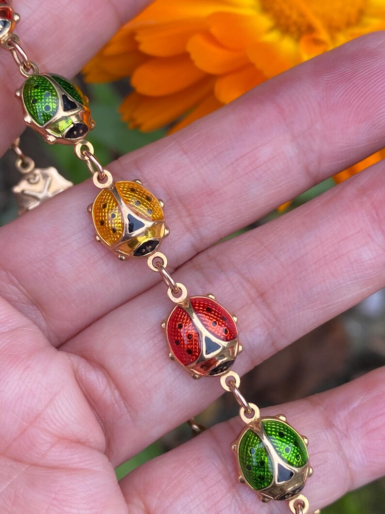 May include: A gold chain bracelet with a series of enamel ladybug charms. The ladybugs are red, green, and yellow with black spots.