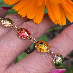 May include: A gold chain bracelet with four enamel ladybug charms. The ladybugs are red, yellow, green, and white with black spots.