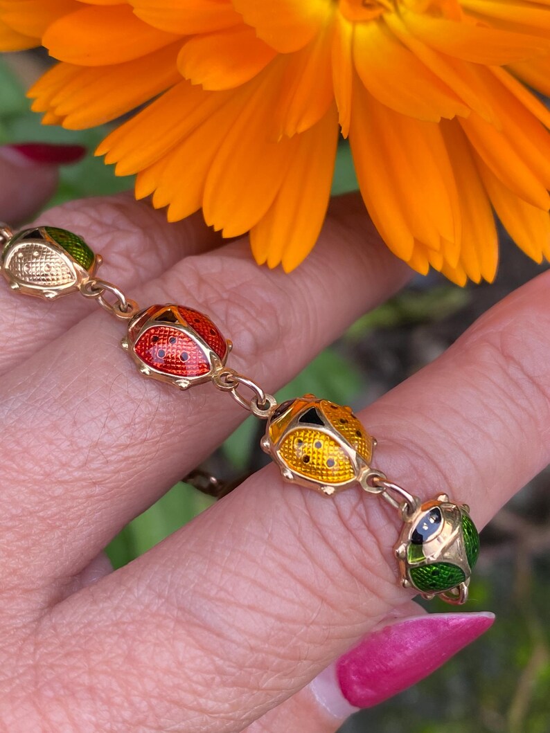 May include: A gold chain bracelet with four enamel ladybug charms. The ladybugs are red, yellow, green, and white with black spots.