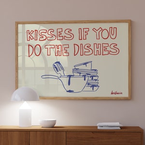 Può includere: Un'opera d'arte da parete rettangolare incorniciata con uno sfondo beige chiaro e testo rosso che recita KISSES IF YOU DO THE DISHES. Sotto il testo c'è un disegno a linee blu di una pila di piatti sporchi, una padella e una spatola.