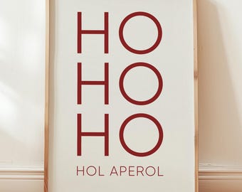 May include: A framed wall art print featuring the text HO HO HO in large, bold, dark red capital letters, with the smaller text HOL APEROL printed in a matching dark red font directly underneath, all set against a plain off-white background.