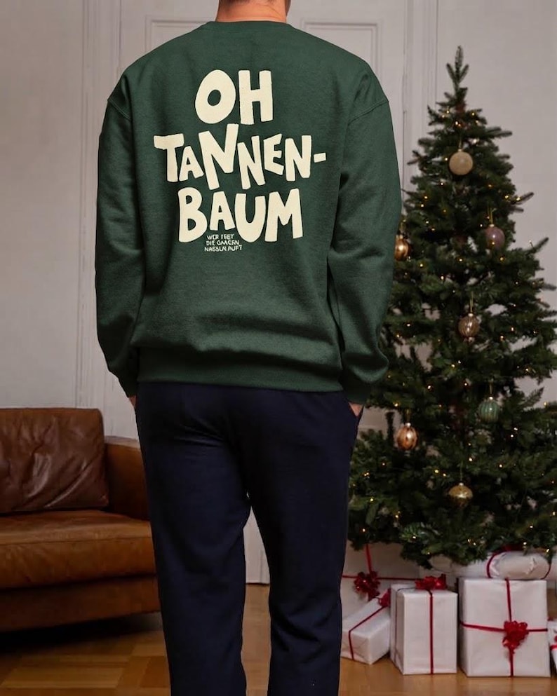 May include: A dark green long-sleeve crewneck sweatshirt featuring the cream-colored text "OH TANNEN-BAUM" printed on the back, with smaller text underneath that reads "WER FEET DIE GANSEN NASSEN PUPT". The sweatshirt has a ribbed collar and cuffs.