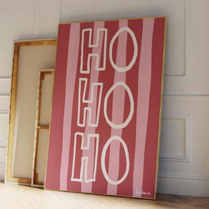 May include: A pink and white striped canvas print with the word "HO HO HO" written in white. The print has a gold frame.