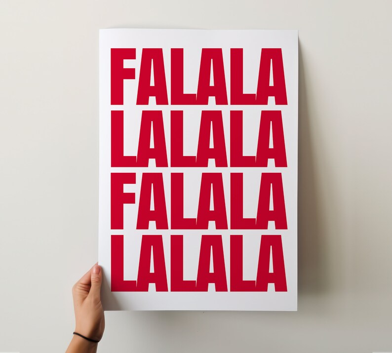 May include: A white poster with the words "FALALA LALALA FALALA LALALA" printed in bold, red letters. The poster is held by a person's hand against a white background. The design is simple and festive.