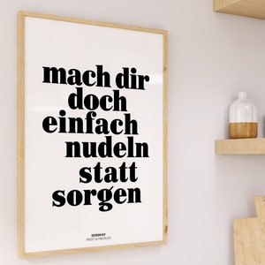 Pu&ograve; includere: Una stampa incorniciata con il testo "mach dir doch einfach nudeln statt sorgen" in lettere nere in grassetto su uno sfondo bianco. Il testo &egrave; centrato sulla stampa. La stampa &egrave; incorniciata in una cornice di legno chiaro.