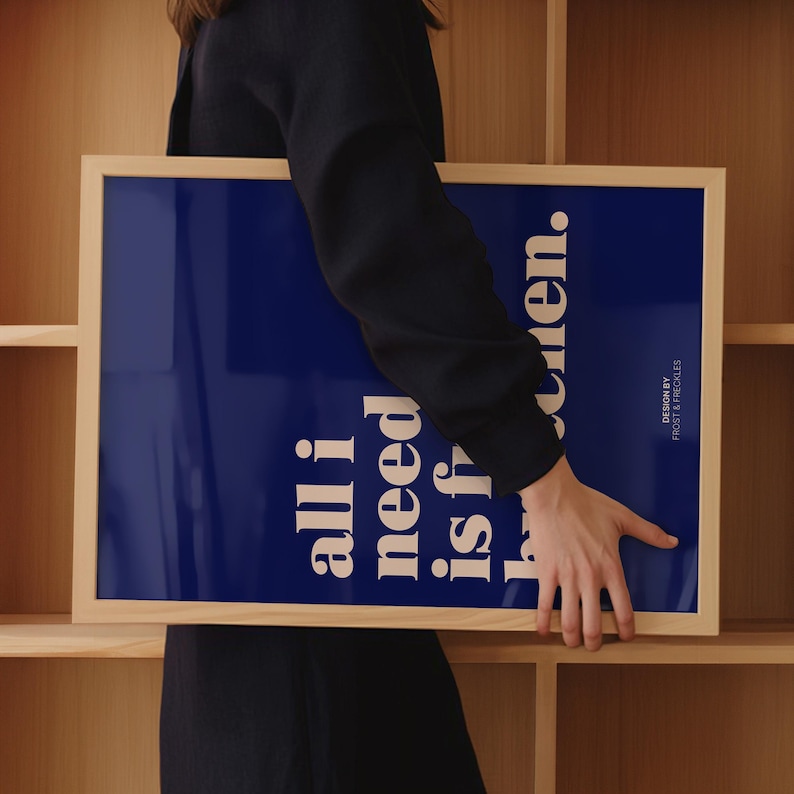 May include: A rectangular framed print with a dark blue background and white text that reads all i need is h...en. The text is arranged vertically in a bold, sans-serif font. The frame is made of light-colored wood with a smooth, natural finish.