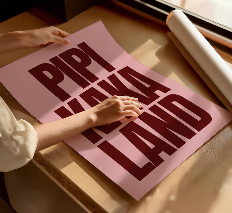 Peut inclure: Une affiche rose avec les mots "PIPI KAKA LAND" en gras, rouge fonc&eacute;. L'affiche est pos&eacute;e sur une surface en bois pr&egrave;s d'une fen&ecirc;tre. Un rouleau de papier blanc est &eacute;galement visible.