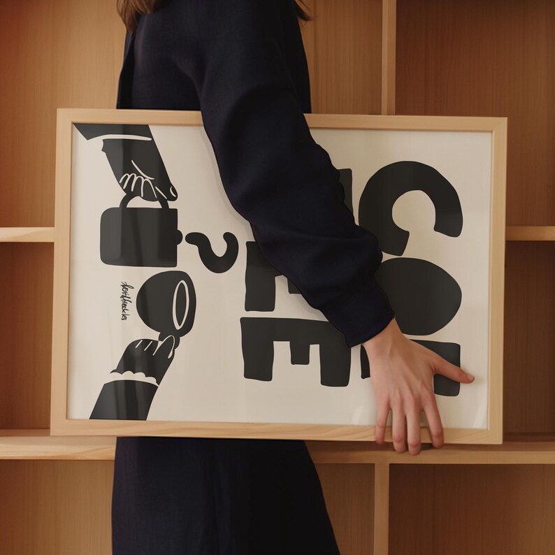 May include: A framed black and white illustration of a hand pouring coffee into a cup. The text "Coffee" is written in large, bold letters. The illustration is on a white background.