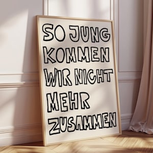 May include: A framed art print with the German text "SO JUNG KOMMEN WIR NICHT MEHR ZUSAMMEN" in bold black letters on a cream background. The print is in a light wood frame, leaning against a white wall.