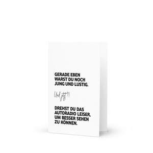 May include: A white card with black text that reads "GERADE EBEN WARST DU NOCH JUNG UND LUSTIG. Und jetzt?! DREHST DU DAS AUTORADIO LEISER, UM BESSER SEHEN ZU K&Ouml;NNEN."