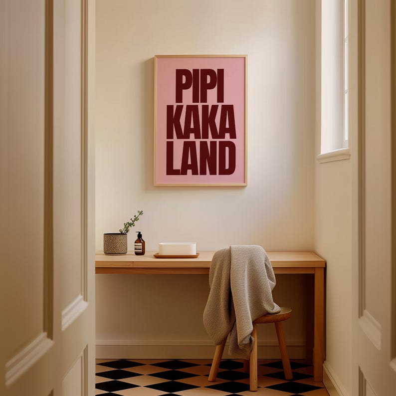 Peut inclure: Une affiche rose encadr&eacute;e avec les mots "PIPI KAKA LAND" en lettres rouge fonc&eacute; est accroch&eacute;e au-dessus d'un bureau en bois. Une petite chaise en bois avec une couverture beige est devant le bureau. Un pot &agrave; motifs et un distributeur de savon sont sur le bureau.