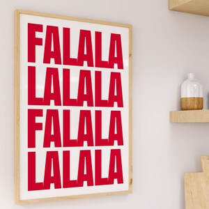 May include: A framed art print with the words "FALALA LALALA FALALA LALALA" in bold red letters on a white background. The frame is a light wood color, and the print is displayed on a white wall.