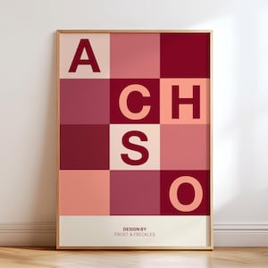 May include: Framed art print featuring a grid of squares in varying shades of red and pink. Large, bold letters spell out "ACHSO" across the squares. The bottom of the print reads "DESIGN BY FROST & FRECKLES".