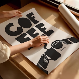 May include: A white poster with black text that reads "COFFEE" in a stylized font. The poster also features a black silhouette of a hand pouring coffee from a mug into another cup.