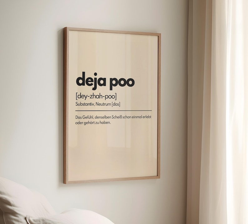 May include: A framed print with the words "deja poo" in a bold, black font. Below the title is the phonetic pronunciation and a German definition. The print is in a light wood frame and hangs on a white wall.