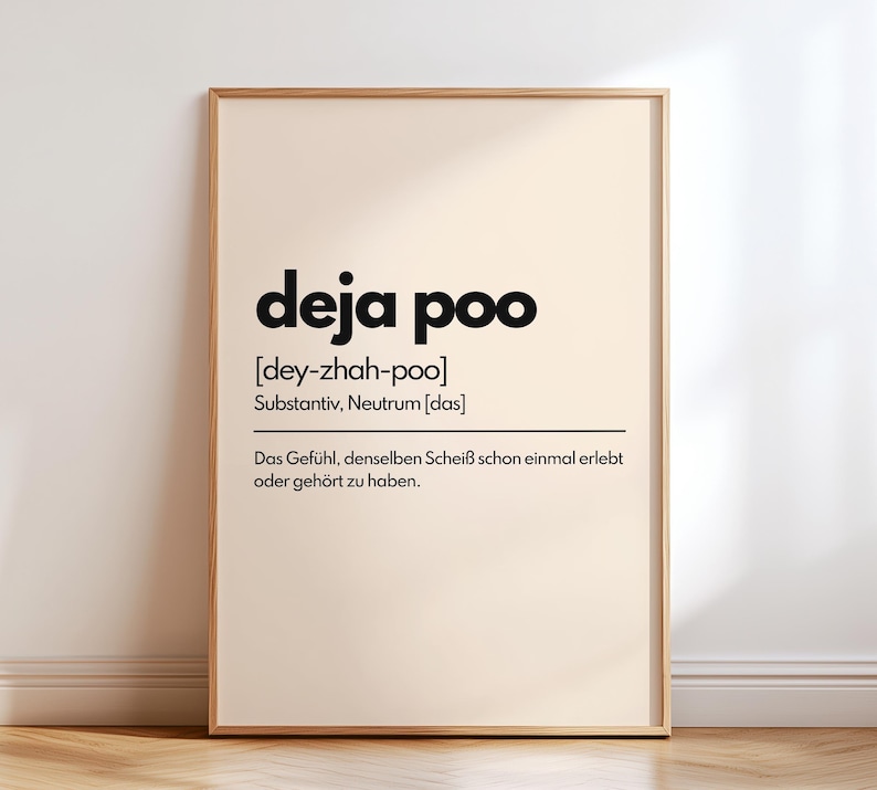 May include: A framed print with the words "deja poo" in bold black font. Below the title is the phonetic pronunciation and a German definition. The print has a light beige background and a wooden frame, suitable for wall decor.
