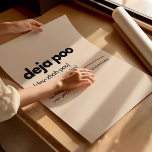 May include: A poster with the words "deja poo" in large black letters. The poster also includes the phonetic pronunciation and a German phrase. The poster is being held by a person.