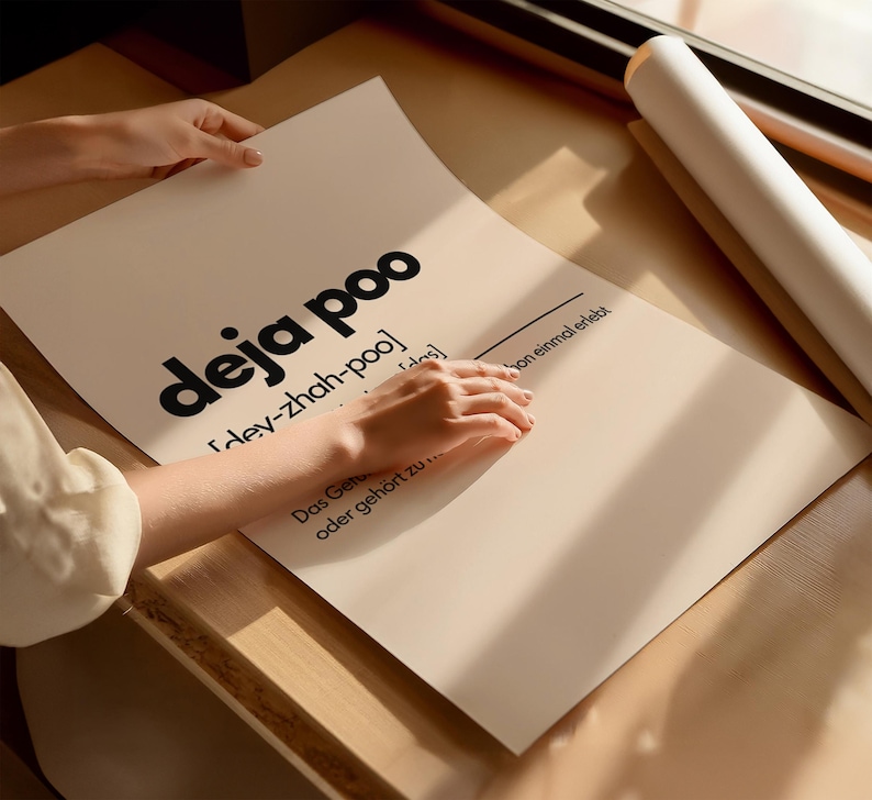 May include: A poster with the words "deja poo" in large black letters. The poster also includes the phonetic pronunciation and a German phrase. The poster is being held by a person.