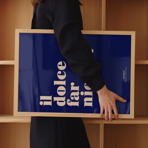 May include: A rectangular framed print with a deep blue background and cream-colored text that reads Il dolce far niente. The design includes the small vertical text Design by Frost & Freckles on the right side, encased in a light wood frame.