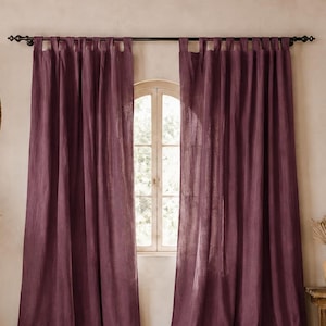 May include: A pair of deep plum-colored curtains with tab-top headers hanging from a dark metal rod. The curtains are made of a textured fabric and extend from the ceiling to the floor, framing a central window with a light-colored wall behind.