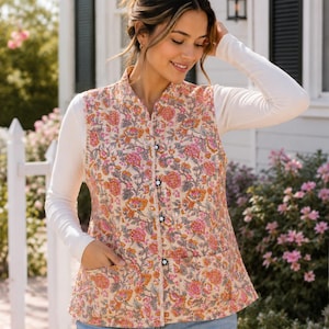 May include: A sleeveless quilted vest featuring a vibrant floral pattern in shades of orange, pink, and green on a cream background. The vest has a high collar, a front button closure with dark circular buttons, and two large patch pockets at the waist.