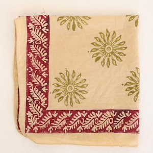 May include: A square textile piece in a light beige color featuring a dark red border with a repeating leaf pattern. The center of the fabric is decorated with a scattered print of olive green sunburst or floral motifs across the surface.