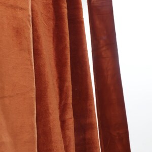 May include: Close-up of a set of rust-colored velvet curtains hanging from a metal rod.