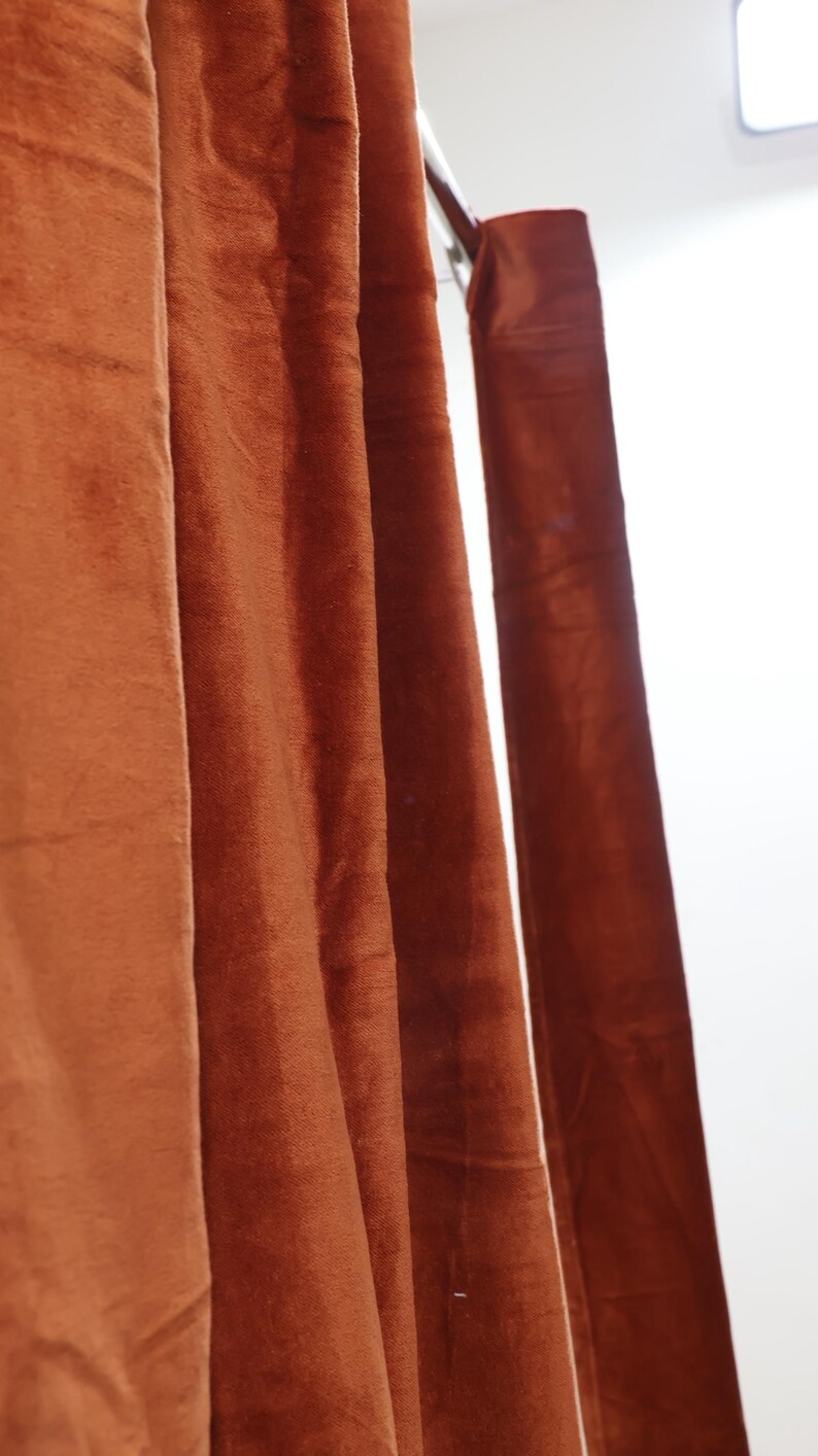 May include: Close-up of a set of rust-colored velvet curtains hanging from a metal rod.