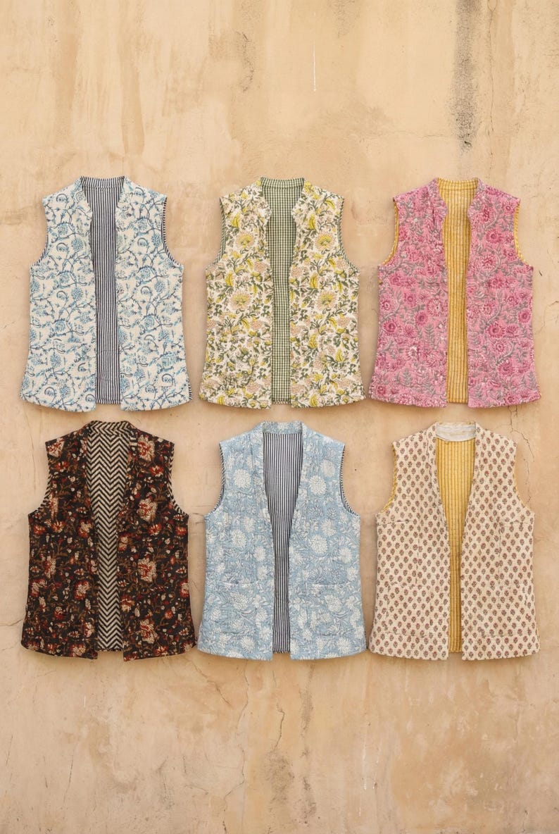 May include: Six reversible vests with floral and geometric patterns. The vests feature various color combinations, including blue, pink, yellow, and brown. Each vest has a different pattern on the front and back, with a striped or patterned interior.