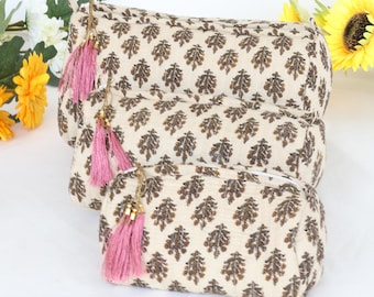 Puede incluir: Tres bolsas de cosméticos de tela beige con estampado de hojas marrones y borlas rosas. Las bolsas están anidadas una dentro de la otra, con la bolsa más grande en la parte superior y la más pequeña en la parte inferior.
