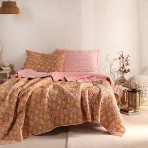 May include: A quilted bedspread featuring a vibrant orange and green floral block print pattern, paired with matching pillowcases. One pillowcase displays the same floral design, while the other features a fine red and white striped pattern.