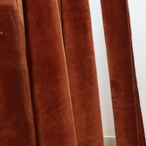 May include: Close-up of a rust-colored velvet curtain with soft folds and texture.