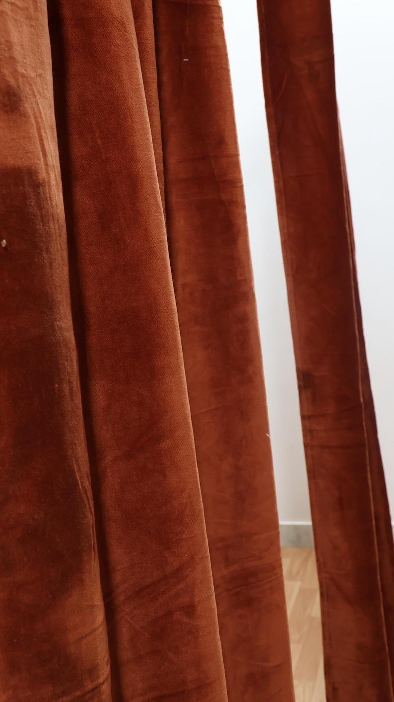 May include: Close-up of a rust-colored velvet curtain with soft folds and texture.