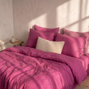 May include: A magenta linen bedding set featuring a duvet cover and four pillowcases, including two standard magenta pillowcases with side button closures and one small rectangular cream-colored textured accent pillow placed in the center.