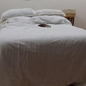 May include: A white linen duvet cover with a white pillow on top. The duvet cover is on a bed with a white sheet underneath. The bed is made and the duvet cover is smooth.