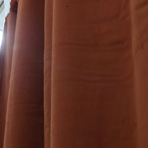 May include: Three brown velvet curtains hanging from a white curtain rod.