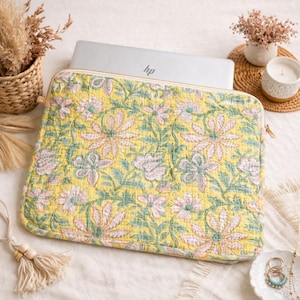 Könnte beinhalten: Gelbe Laptop-Hülle mit floralem Muster und Steppdesign. Die Hülle hat einen Reißverschluss und ein Muster aus großen rosa und grünen Blumen auf gelbem Grund. Ein HP-Laptop befindet sich in der Hülle.