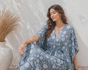 May include: A floor-length blue kaftan dress featuring a white floral pattern, a V-neckline, and a cinched waist with a drawstring detail. The garment has loose, wide sleeves and a flowing skirt that drapes down to the floor in a relaxed silhouette.