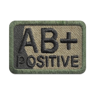Könnte beinhalten: Ein grüner und brauner gestickter Aufnäher mit schwarzen Nähten, auf dem "AB+ POSITIV" steht.