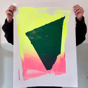 May include: A green abstract shape is printed on a white paper background. The shape is surrounded by a yellow and pink gradient.