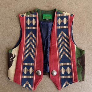 May include: A colorful vest with a Southwestern design. The vest features a red and blue geometric pattern, with silver-colored buttons. The vest has a green collar and a camouflage pattern on the sides.