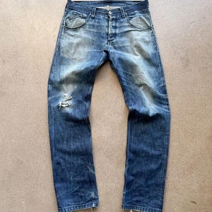 Op de afbeelding: Verbleekte blauwe denim jeans met een distressed look. De jeans hebben een knoopsluiting, een klassiek vijf-zakken ontwerp en een versleten plek op het linkerbeen. De jeans hebben een medium wassing met lichtere plekken en subtiele vervaging.