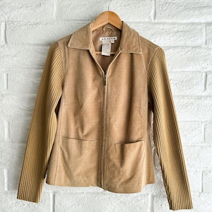 May include: A tan suede jacket featuring a full-length front zipper, a classic collar, and two front patch pockets. The sleeves are made of a ribbed knit fabric in a matching tan color. The interior label displays the text A.M.I.