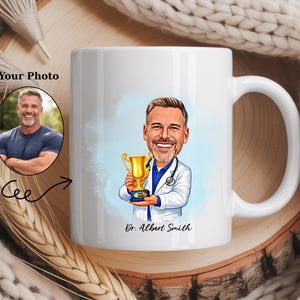 Op de afbeelding: Witte keramische mok met een cartoonillustratie van een dokter die een trofee vasthoudt, met de tekst "Dr. Albert Smith". Aan de linkerkant van de mok staat een foto van een man. De mok heeft een gebogen handvat.
