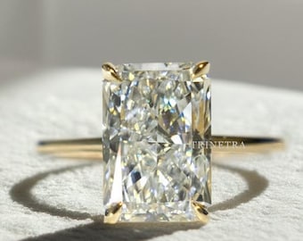 Puede incluir: Un anillo de diamantes de talla rectangular con una banda de oro. El diamante tiene una apariencia clara y brillante. El anillo está sobre una superficie blanca, con un fondo suave.