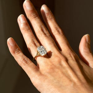May include: A gold ring featuring a large, rectangular, faceted clear gemstone set in a four-prong setting. The band is thin and polished, showcasing a classic design that highlights the brilliance and clarity of the central stone.