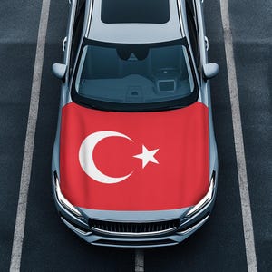 May include: A silver car with a red, white, and crescent moon car cover. The car cover features the Turkish flag.
