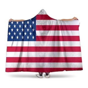 Könnte beinhalten: Eine Kapuzendecke mit dem Design der amerikanischen Flagge. Die Decke hat ein blaues Feld mit weißen Sternen und rot-weißen Streifen. Die Person trägt weiße Schuhe.